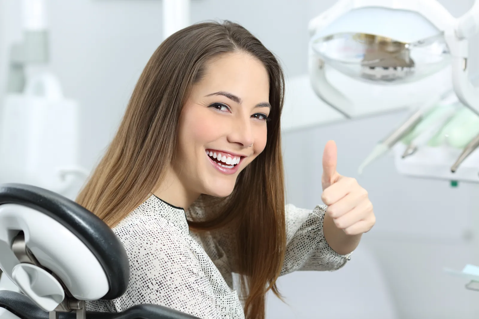 A smiling woman giving a thumbs up from the dental chair