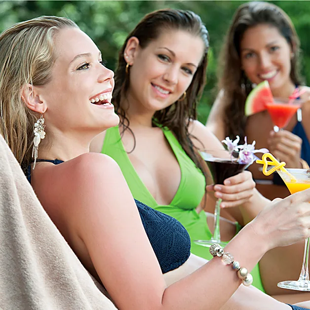 Three women relaxing together poolside with drinks.