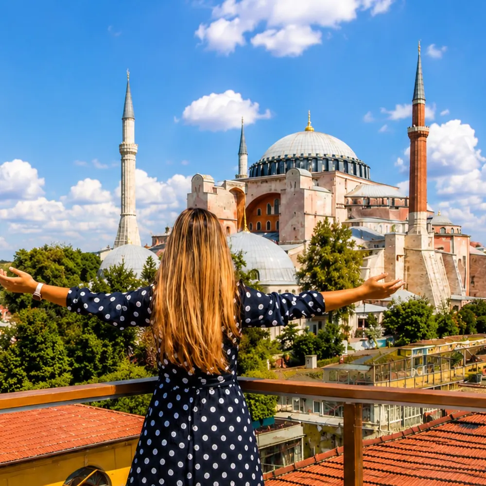 A woman seen from behind on a rooftop terrace, arms open, facing the Hagia Sophia in Istanbul.