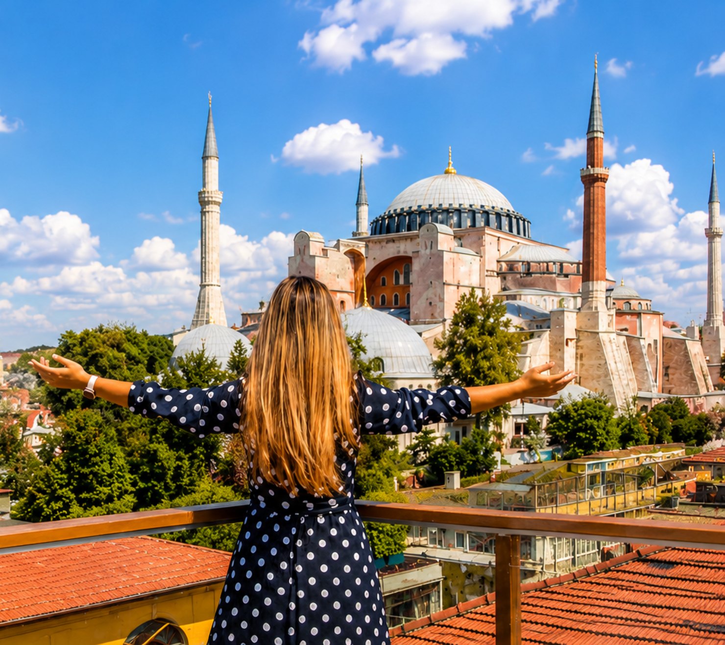 A woman seen from behind on a rooftop terrace, arms open, facing the Hagia Sophia in Istanbul.
